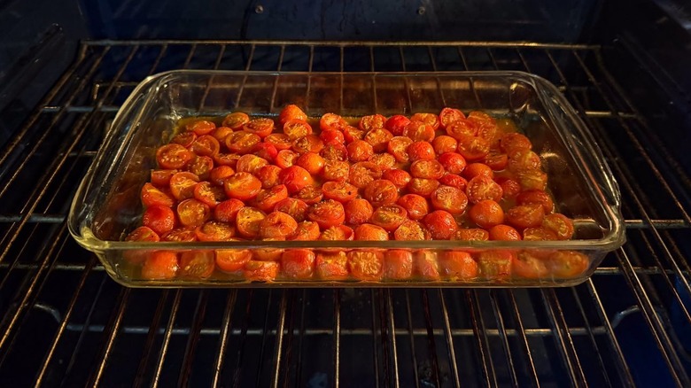 Marinated cherry tomato halves roasting in glass baking dish in oven