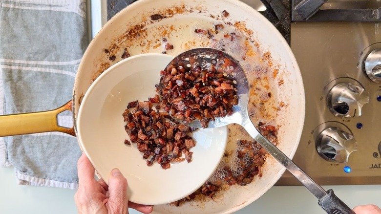 Removing cooked bacon pieces from the rendered fat in a skillet using a slotted spoon