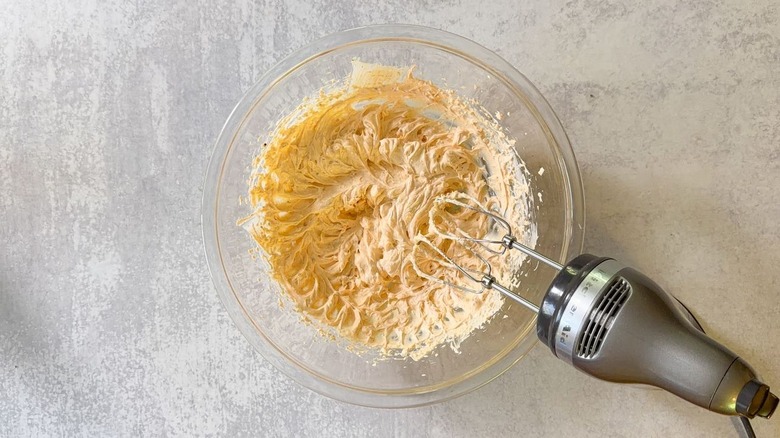 Beaten cream cheese, sour cream, and mayo with seasonings in glass mixing bowl with hand mixer