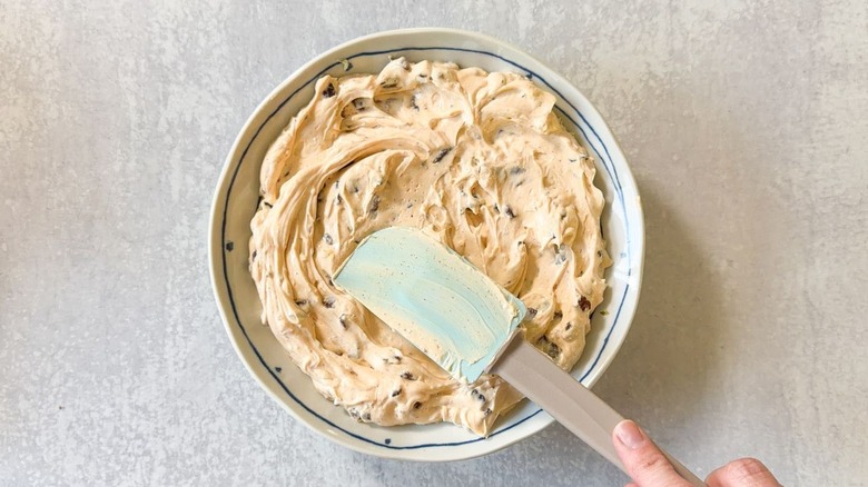Spreading creamy BLT dip base in a shallow bowl with a rubber spatula