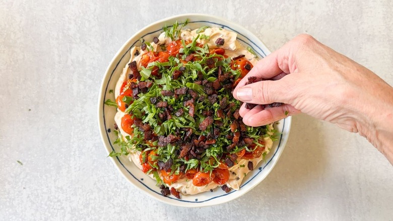 Garnishing BLT dip with chopped arugula, chives, and crisp bacon pieces