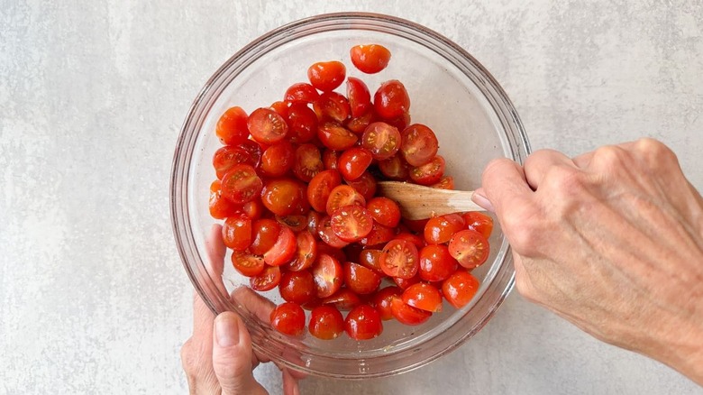 Tossing halved cherry tomatoes with olive oil, vinegar, brown sugar, salt, and pepper in glass bowl