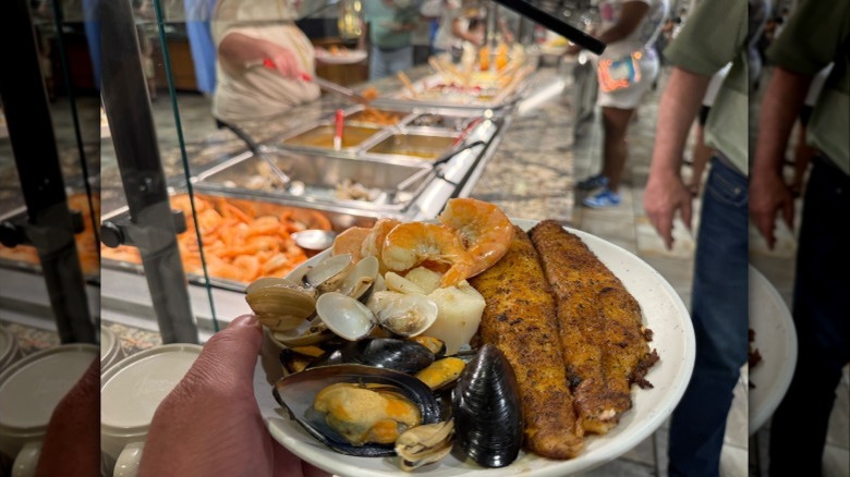 Person holding a plate with various seafood at Shady Maple Smorgasbord