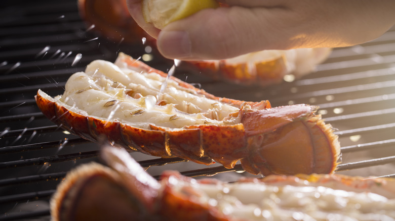lobster tails on the grill, with a hand squeezing lemon juice on top