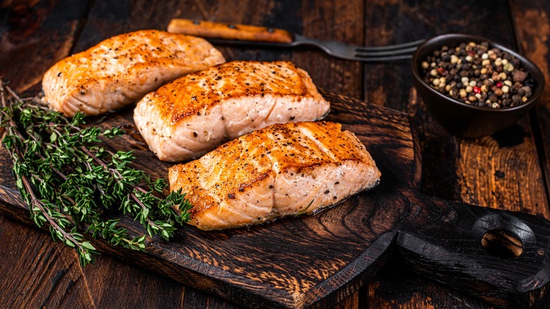 perfectly cooked salmon steaks on a wooden board, served with thyme and peppers