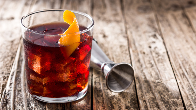 Boulevardier cocktail with an orange peel garnish and a jigger on the side