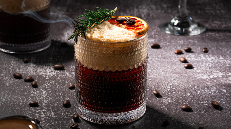 Carajillo cocktail with a burnt rosemary sprig, dehydrated orange slice, and espresso bean garnish