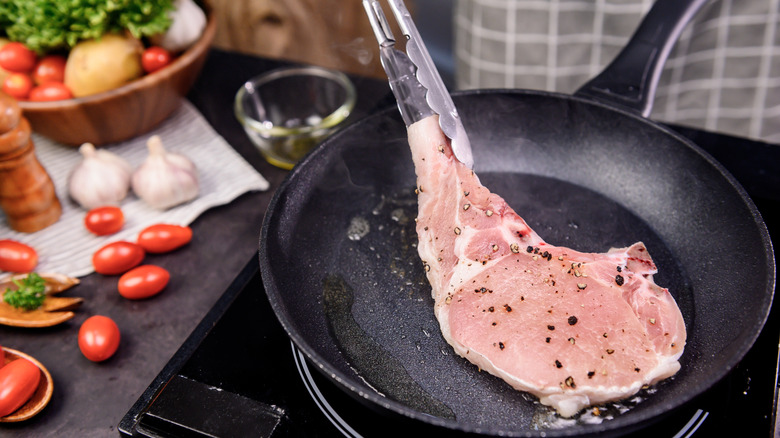 Tongs flip a pork chop in a fry pan.