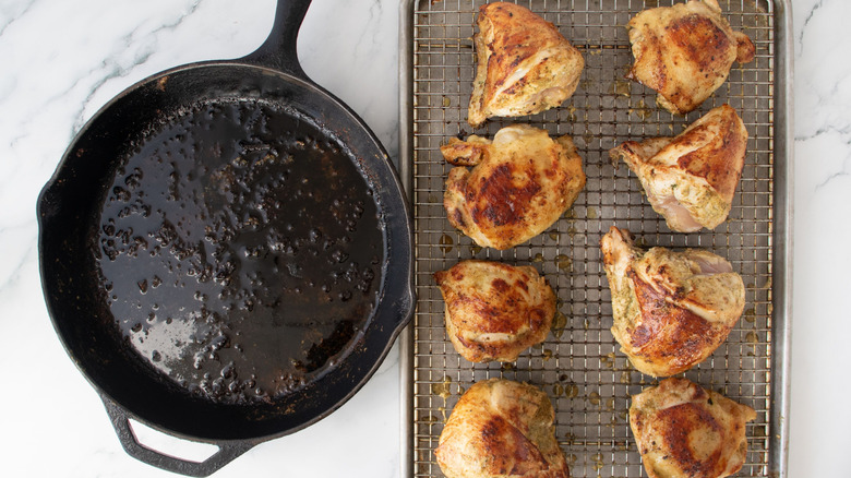 Cast iron skillet next to seared chicken pieces on wire rack