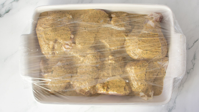 Marinated chicken in casserole dish covered with plastic wrap