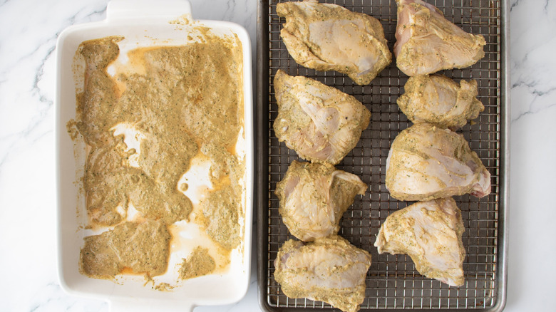 Marinated chicken pieces on wire rack next to casserole dish with excess marinade