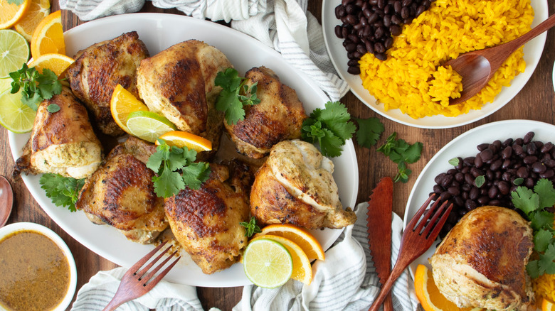 Mojo chicken on platter surrounded by citrus slices, beans, rice, and herbs