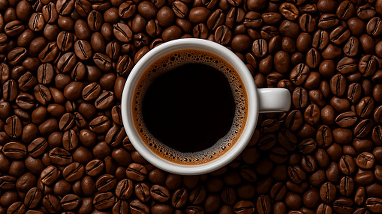 A white cup of black coffee surrounded by coffee beans.
