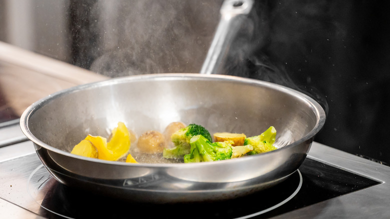 stainless steel pan with vegetables sizzling on stove