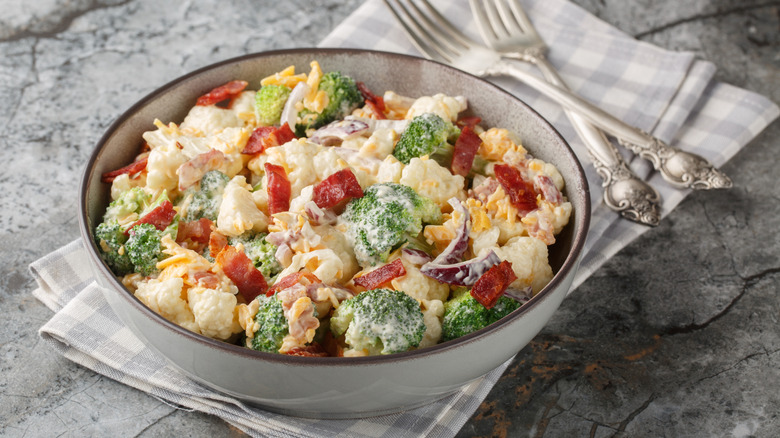 Delicious mayonnaise salad with broccoli, cauliflower, bacon, cheddar cheese and red onion close-up in a bowl on the table.
