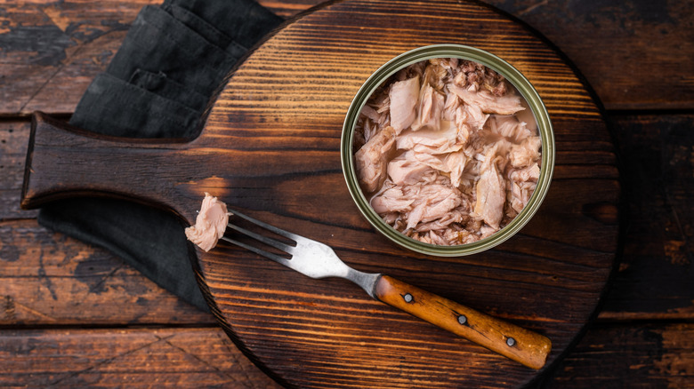 An open can of tuna on a cutting board.