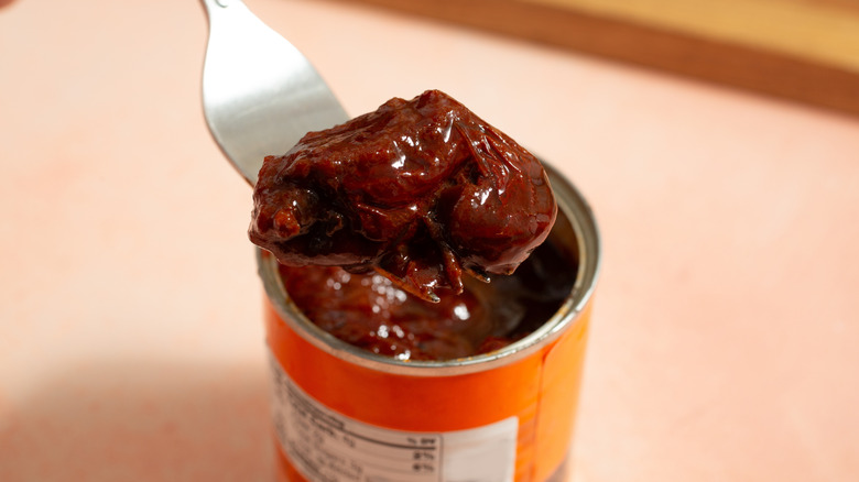 A fork removes a pepper from a can of chipotle peppers in adobo.