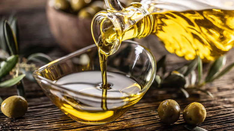 A bottle of olive oil is poured into a small glass bowl.