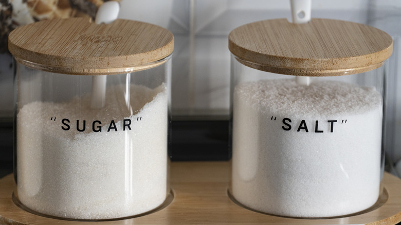 A large glass container of sugar beside another for salt.