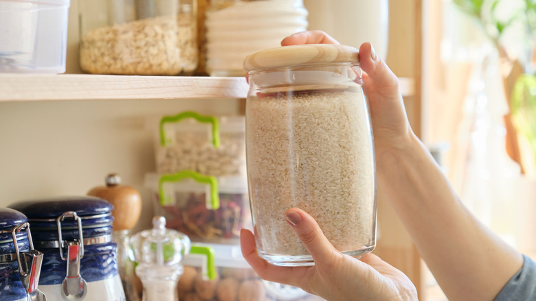 A person's hands are seen holding a glass jar of rice.
