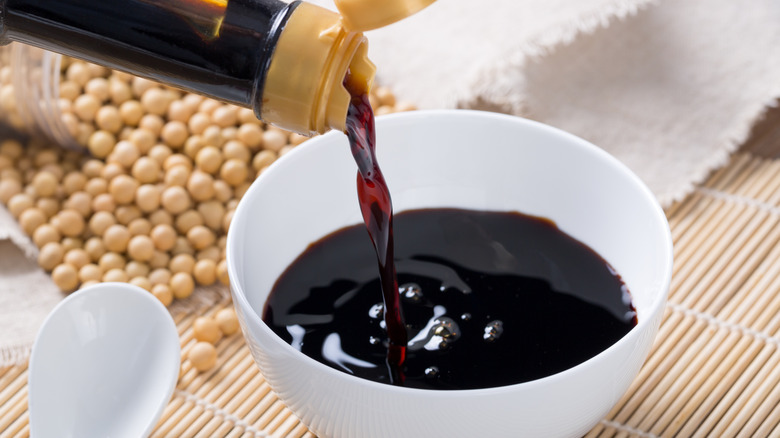 Soy sauce is poured into a white bowl from a bottle.