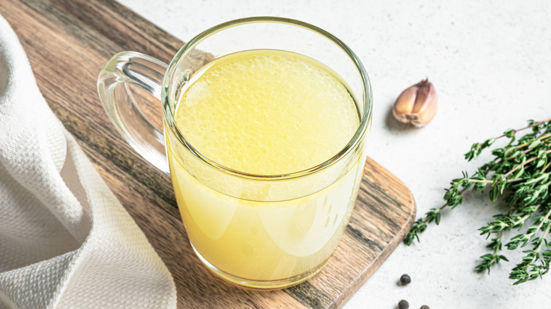 A cup of chicken broth on a wooden cutting board.