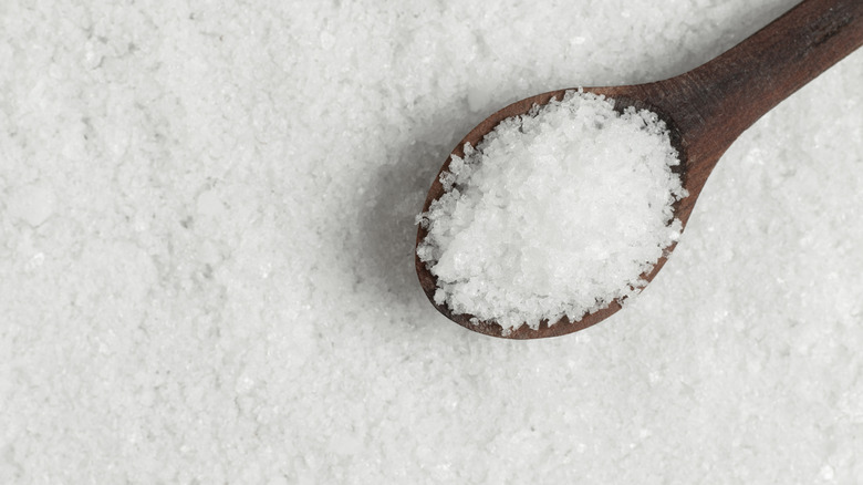 Wooden spoon with salt sitting atop a pile of salt.