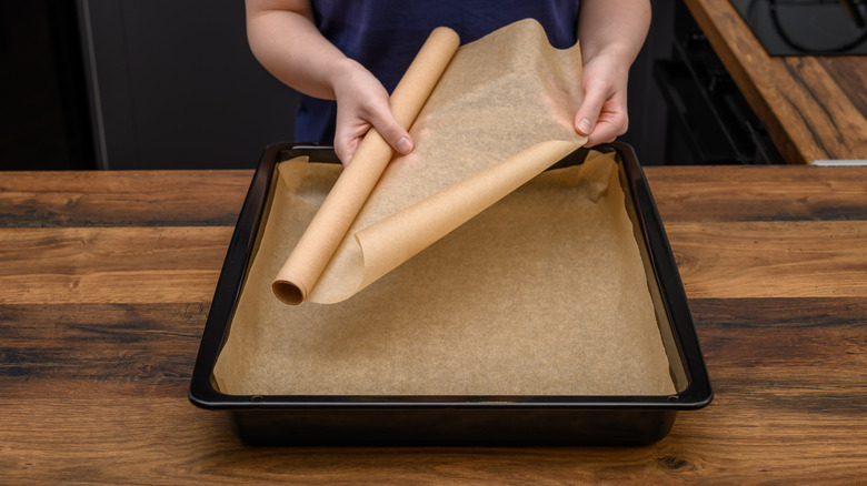 A woman unrolling parchment paper and placing it on a baking tray