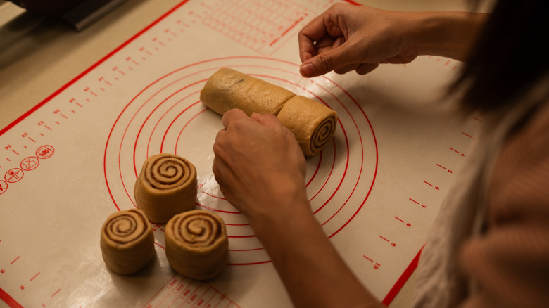 A cook placing unbaked cinnamon rolls on a silicone baking sheet