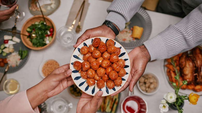 People's hands are seen passing a plate of cocktail meatballs across a table.