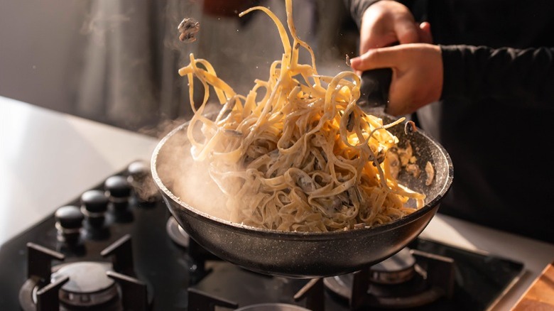 Chef tossing creamy pasta in pan