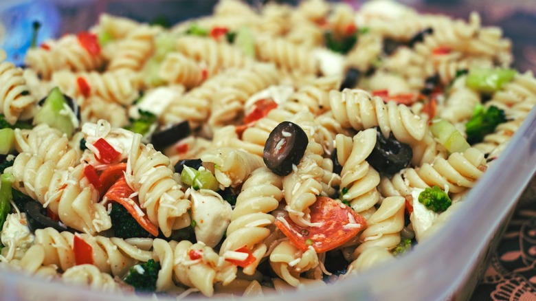 A pasta salad with olives, tomatoes, cucumbers, dressing, and other ingredients