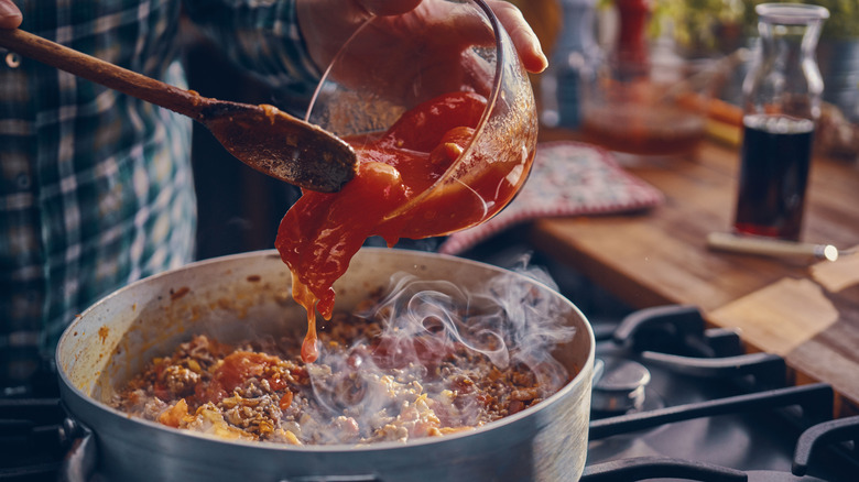 A close-up of a person cooking pasta sauce, pouring tomato sauce into the pot.