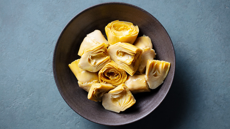 Artichoke hearts in a black bowl on a blue surface.