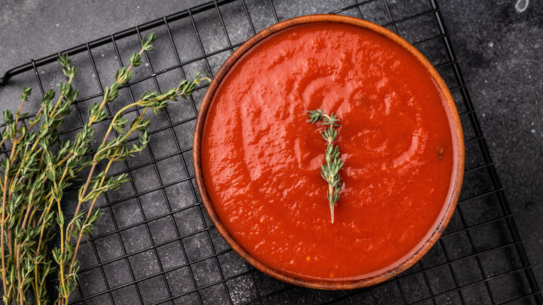 Bowl of tomato sauce on a wire rack with herbs on the side