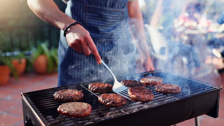 Person flipping burgers on charcoal grill