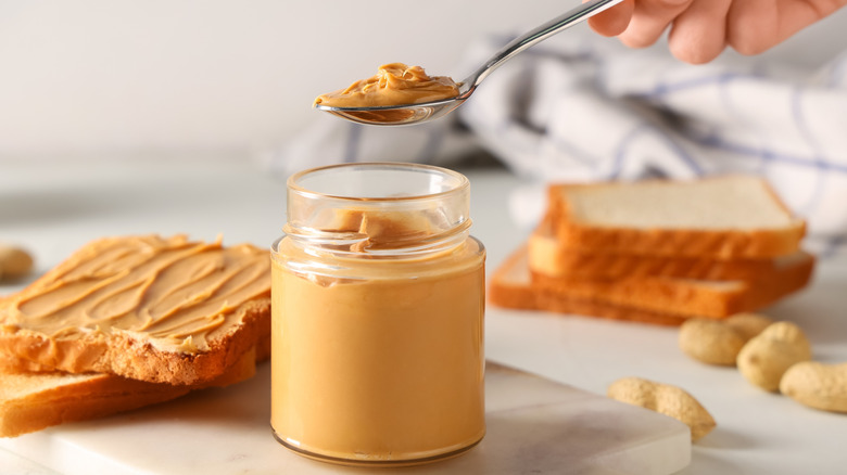 Hand removing a scoop of peanut butter from a jar