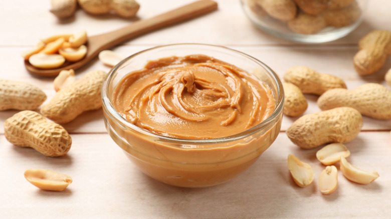 A bowl of creamy peanut butter surrounded by peanuts
