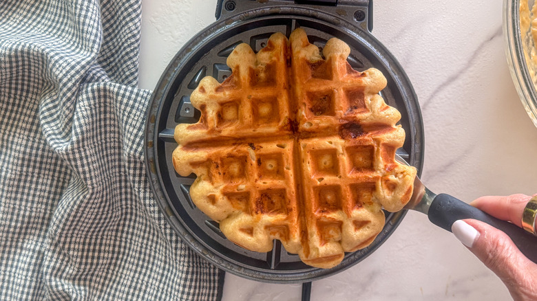 hand using spatula to remove waffle from waffle maker
