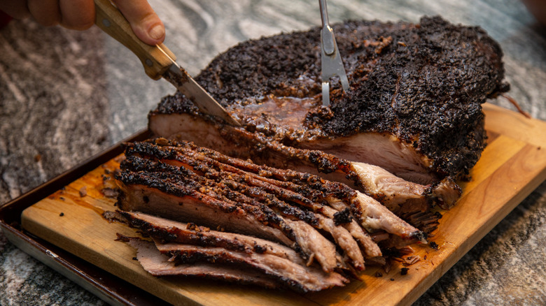 A cooked brisket on a cutting board being sliced