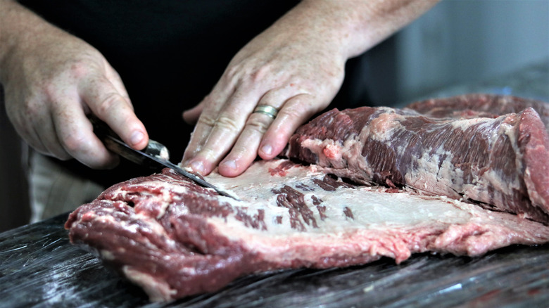 A raw beef brisket being trimmed of extra fat