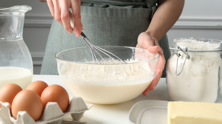 Woman whisking batter in a bowl at a white table indoors, closeup.