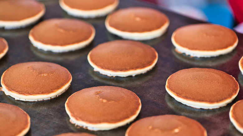 Pancakes cooking in rows on a griddle.