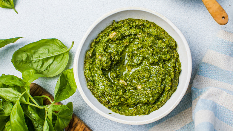 a bowl of pesto with basil leaves in the background