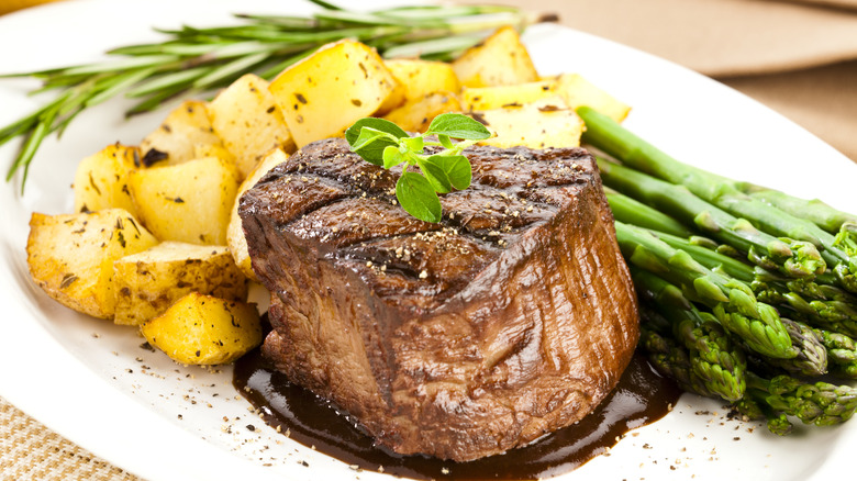 An oval plate with a filet mignon steak, asparagus, and diced potatoes.