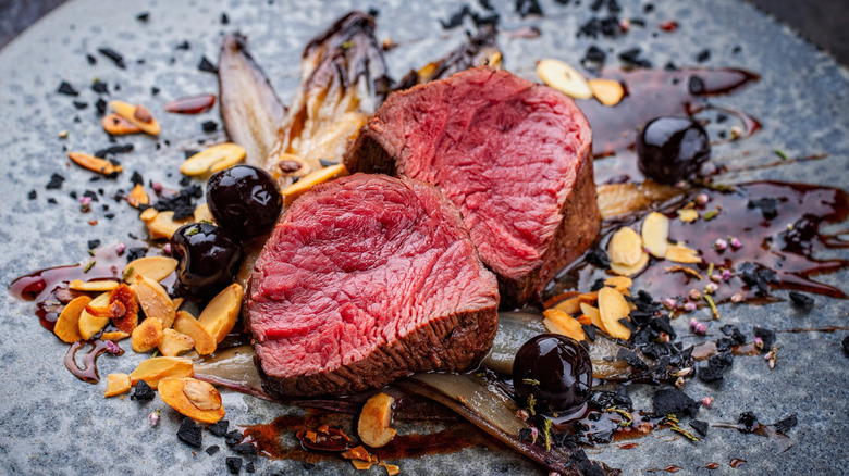 Rare filet mignon medallions on a plate with berries, nuts, and sauce