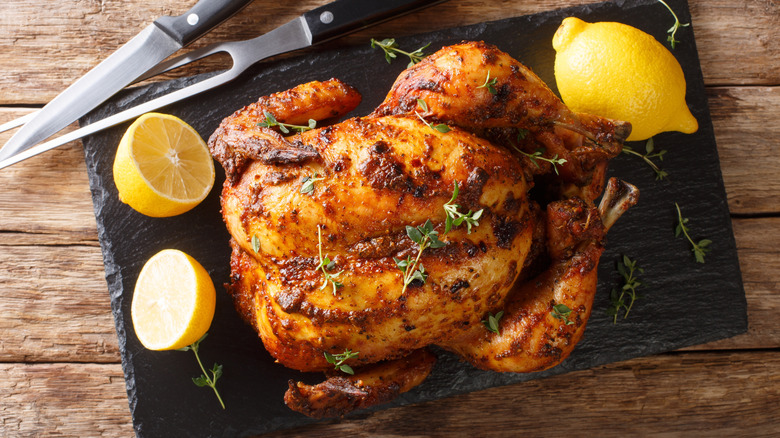 Rotisserie chicken with herbs and lemon on a slate cutting board