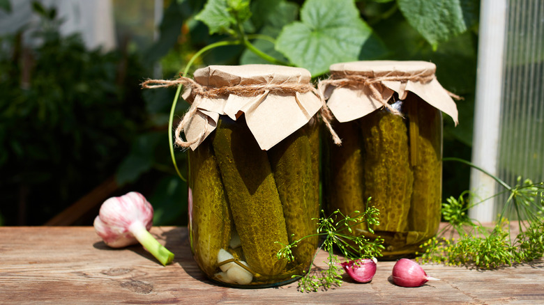 Two jars of homemade pickles sit on a wooden table.