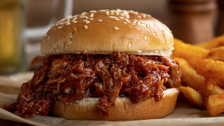 A pulled pork sandwich on a bun next to french fries.