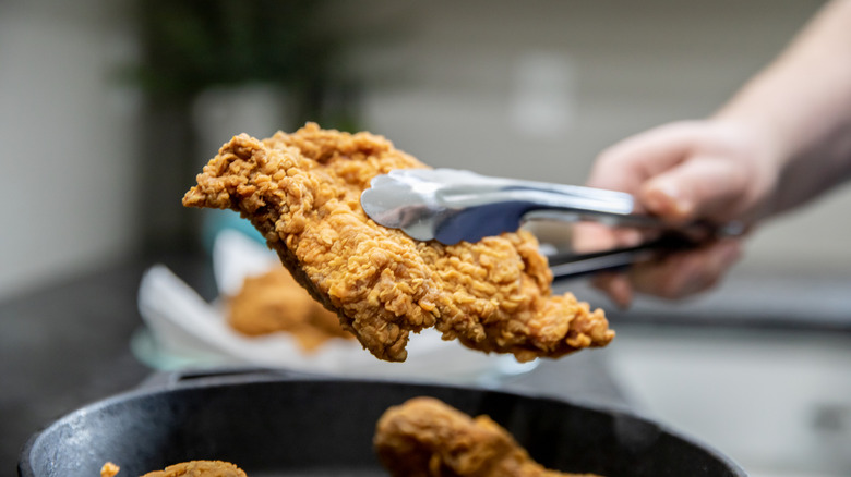 A piece of chicken being held up with tongs